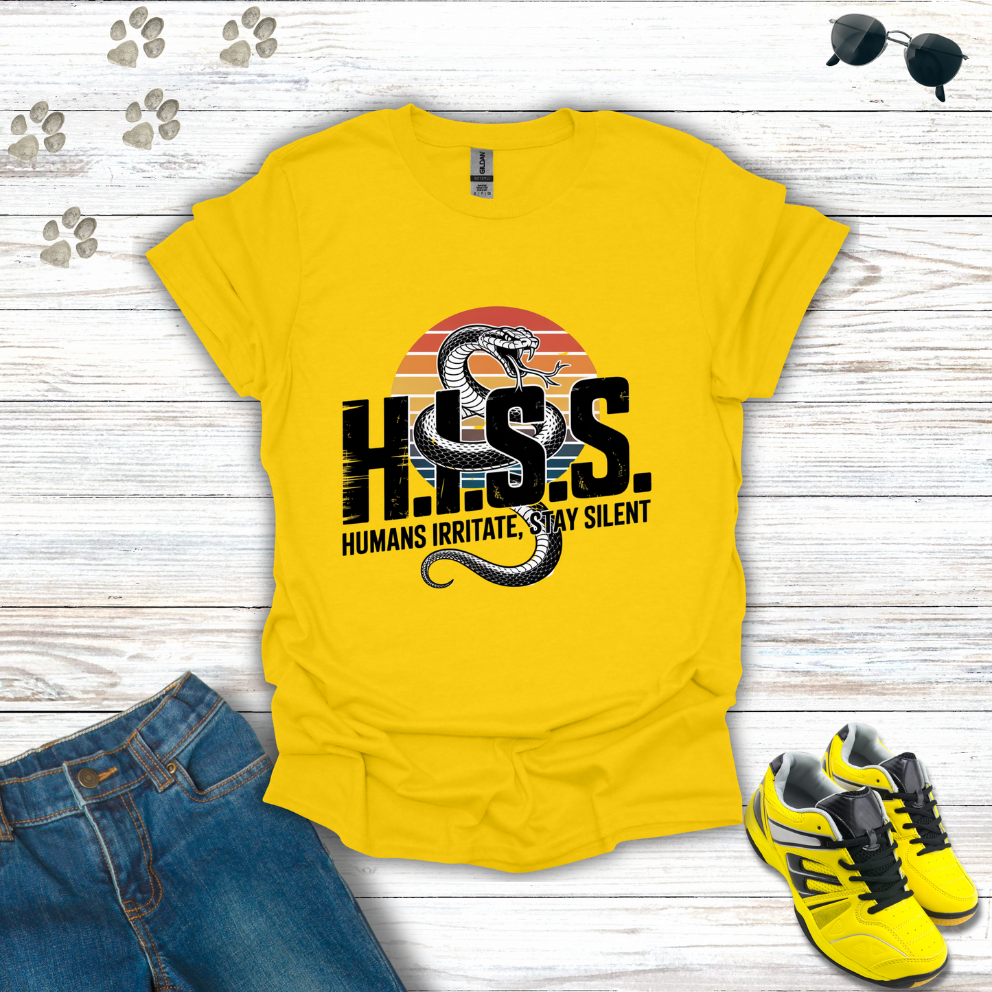Yellow t-shirt with snake graphic and text on a wooden surface with jeans and shoes.