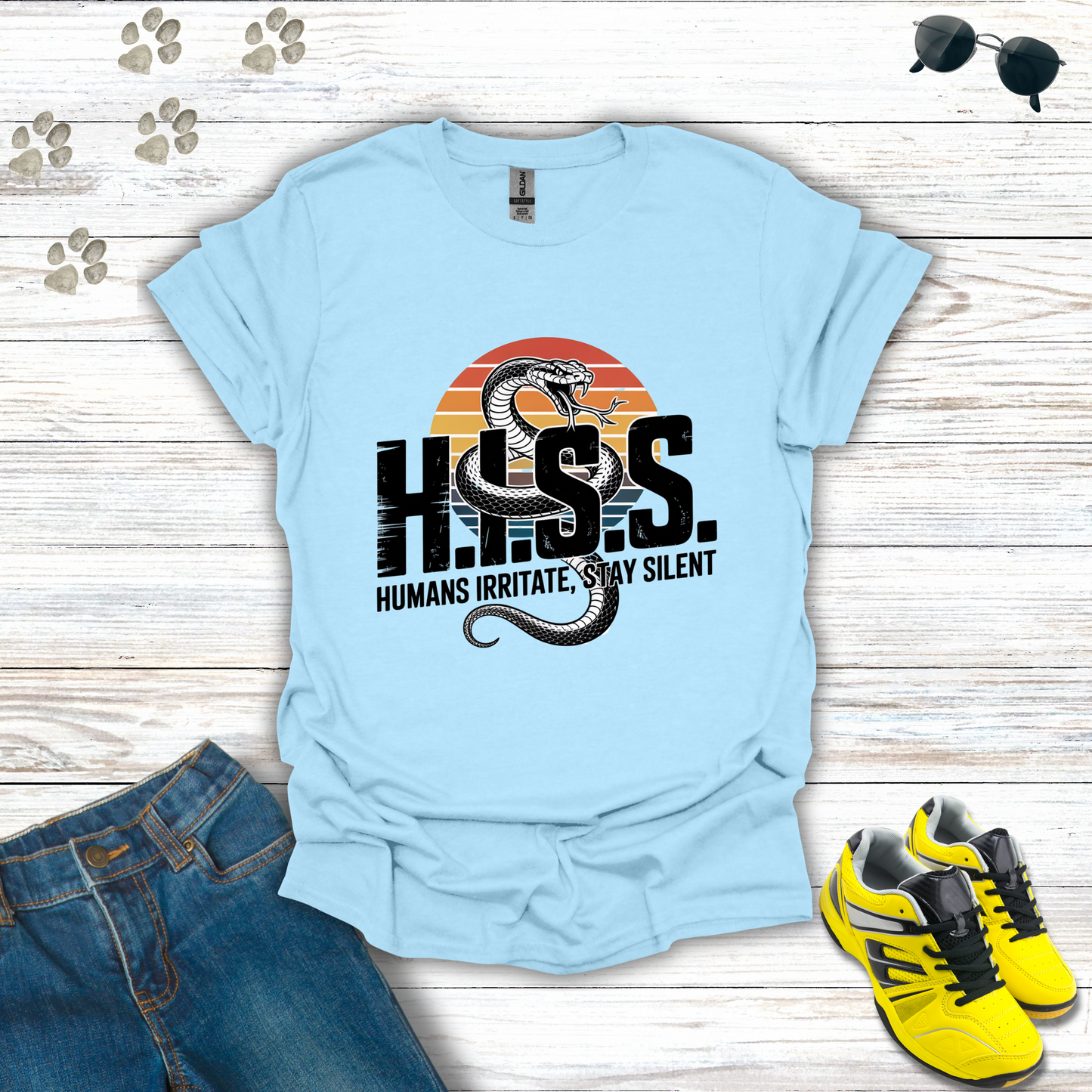 Light blue t-shirt with snake graphic and text on a wooden surface with jeans and sneakers.