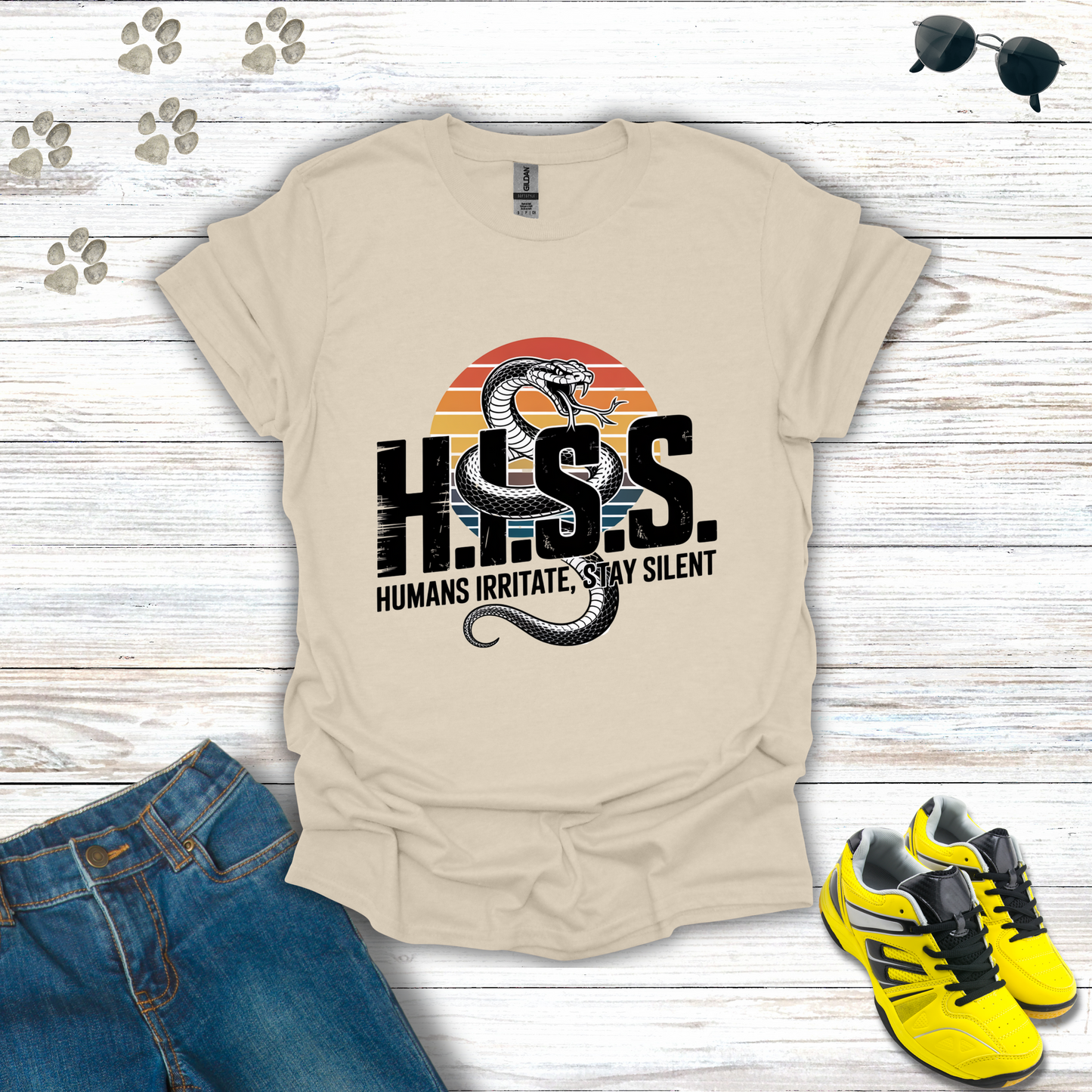 Beige t-shirt with snake graphic and text on a wooden surface with jeans and sneakers.