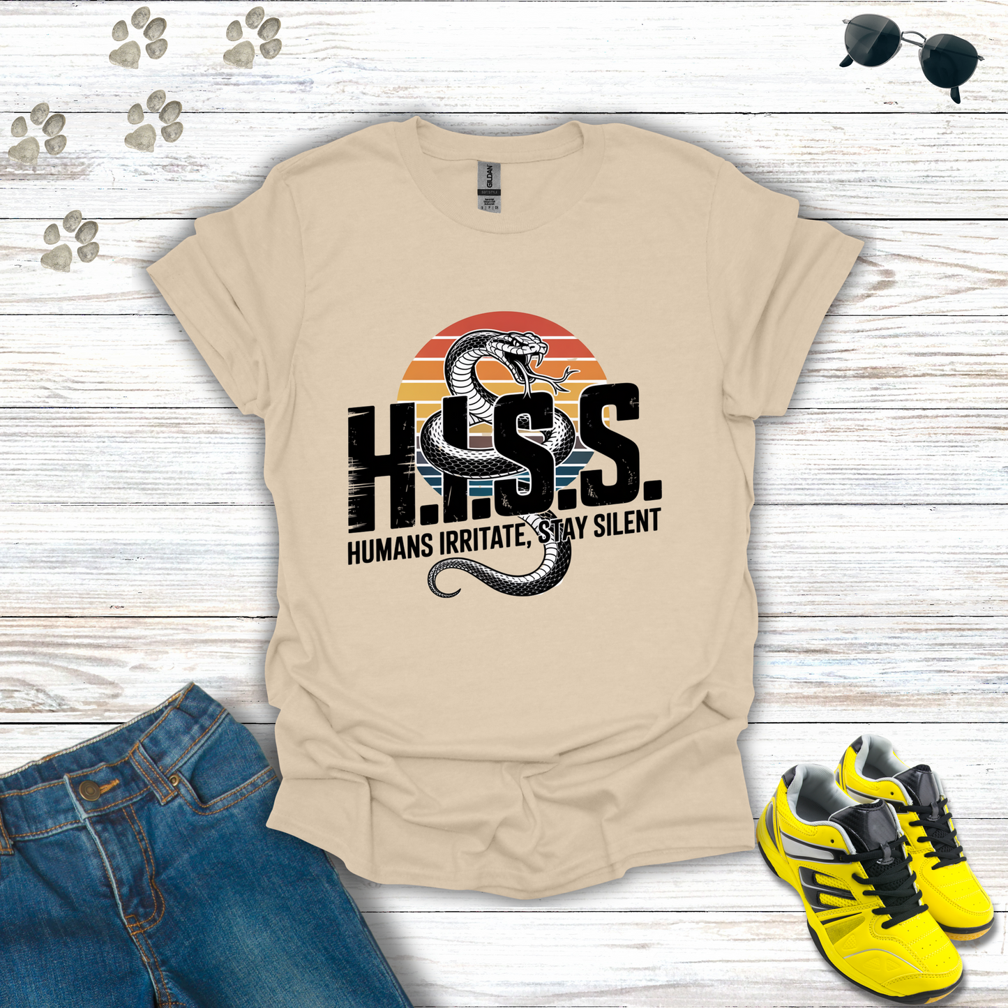 Beige t-shirt with snake graphic and text on a wooden surface with jeans and sneakers.