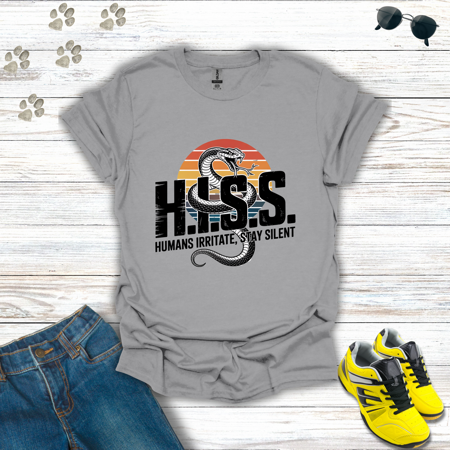 Gray t-shirt with snake graphic and text on a wooden surface with jeans and sneakers.