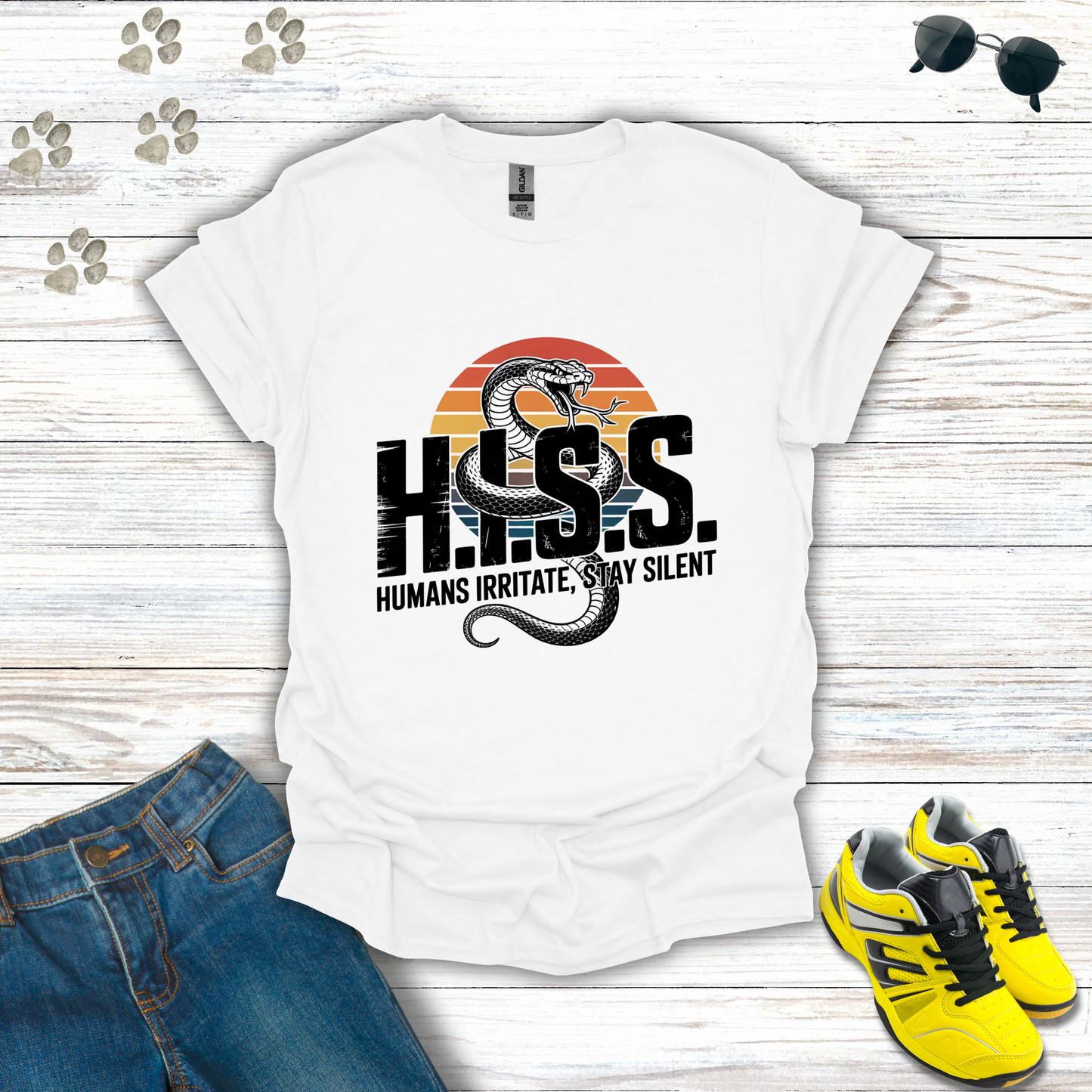 White t-shirt with 'H.H.S.S. Humans Irritate, Stay Silent' design on a wooden surface with jeans and sneakers.