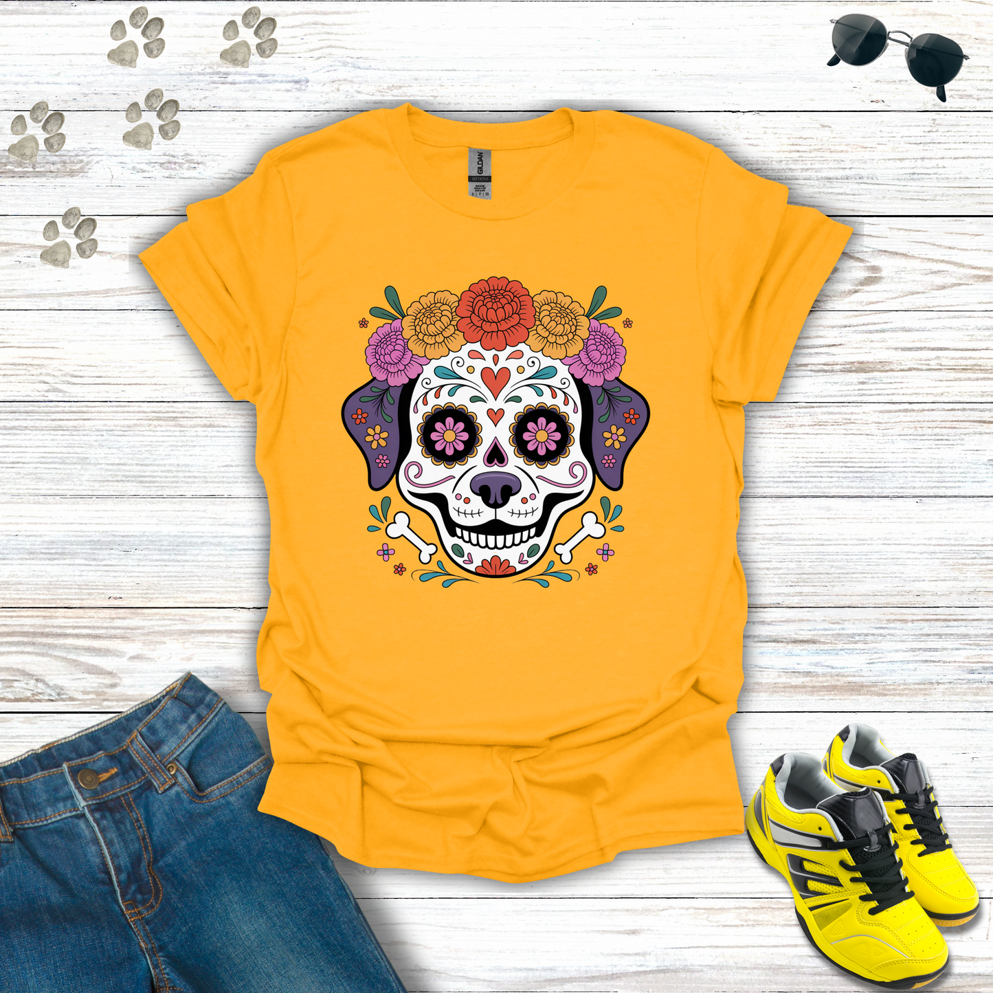 Gold t-shirt with a colorful skull design on a wooden surface with jeans and sneakers.