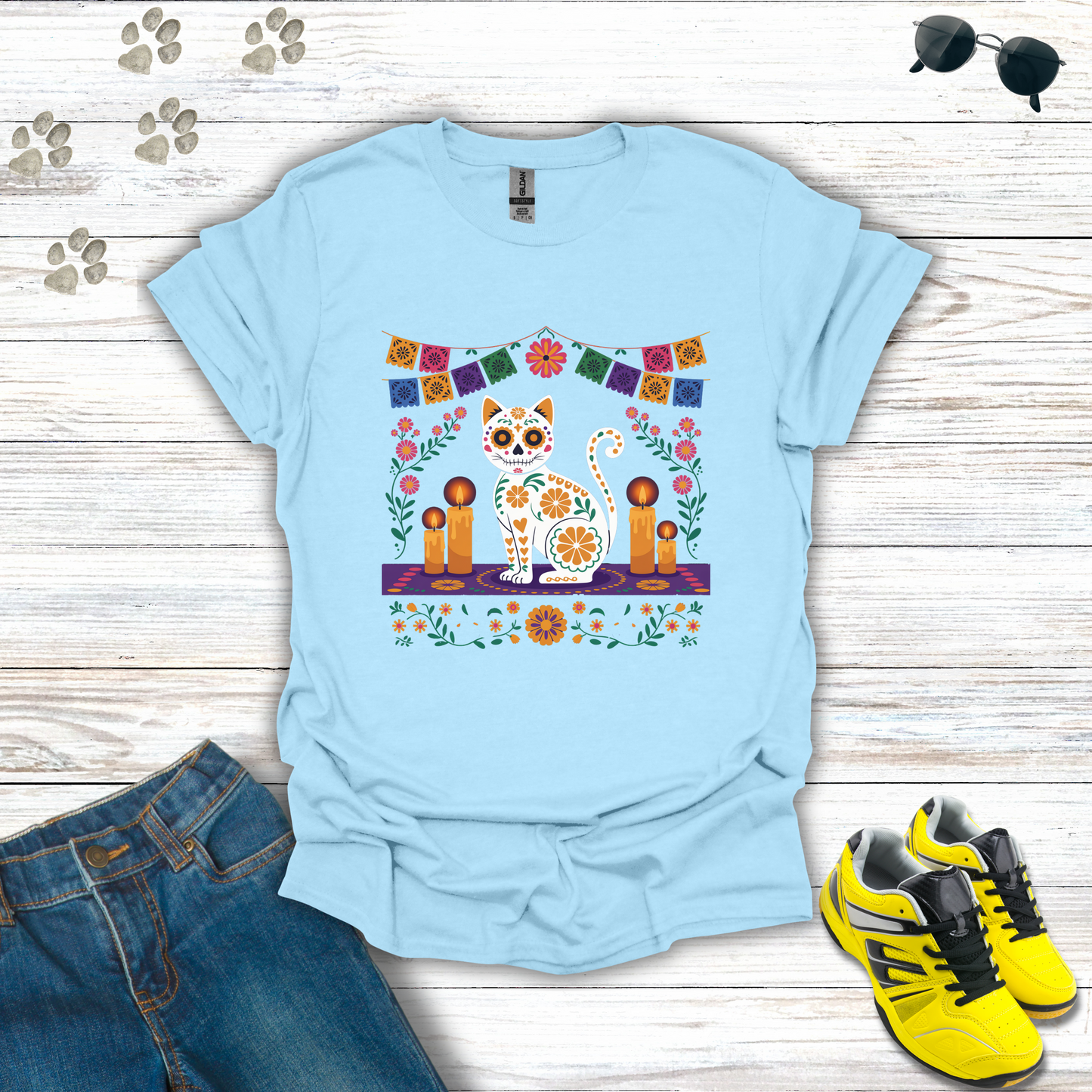 Light blue t-shirt with a colorful graphic design on a wooden surface with jeans and sneakers.