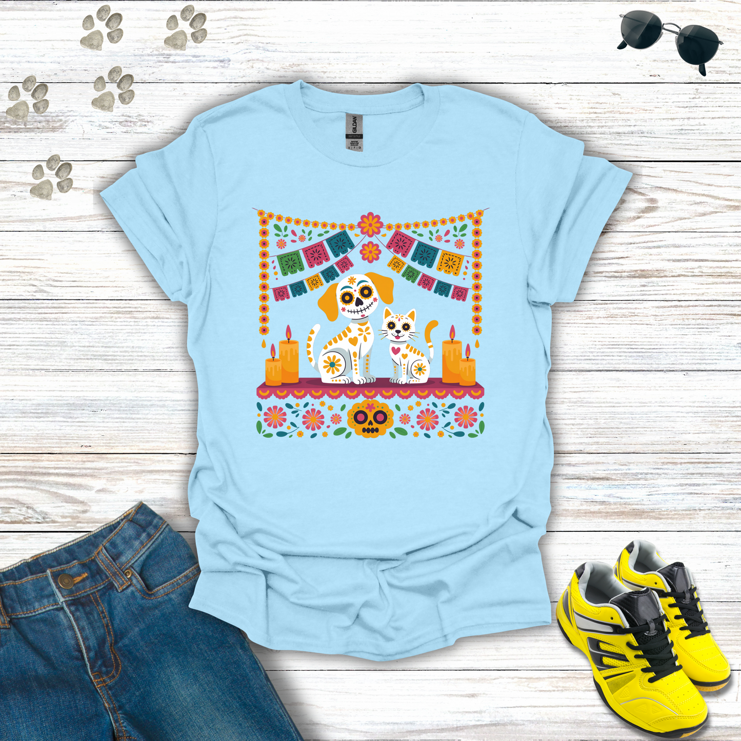 Light blue t-shirt with a colorful graphic of two dogs, jeans, and yellow sneakers on a wooden surface.