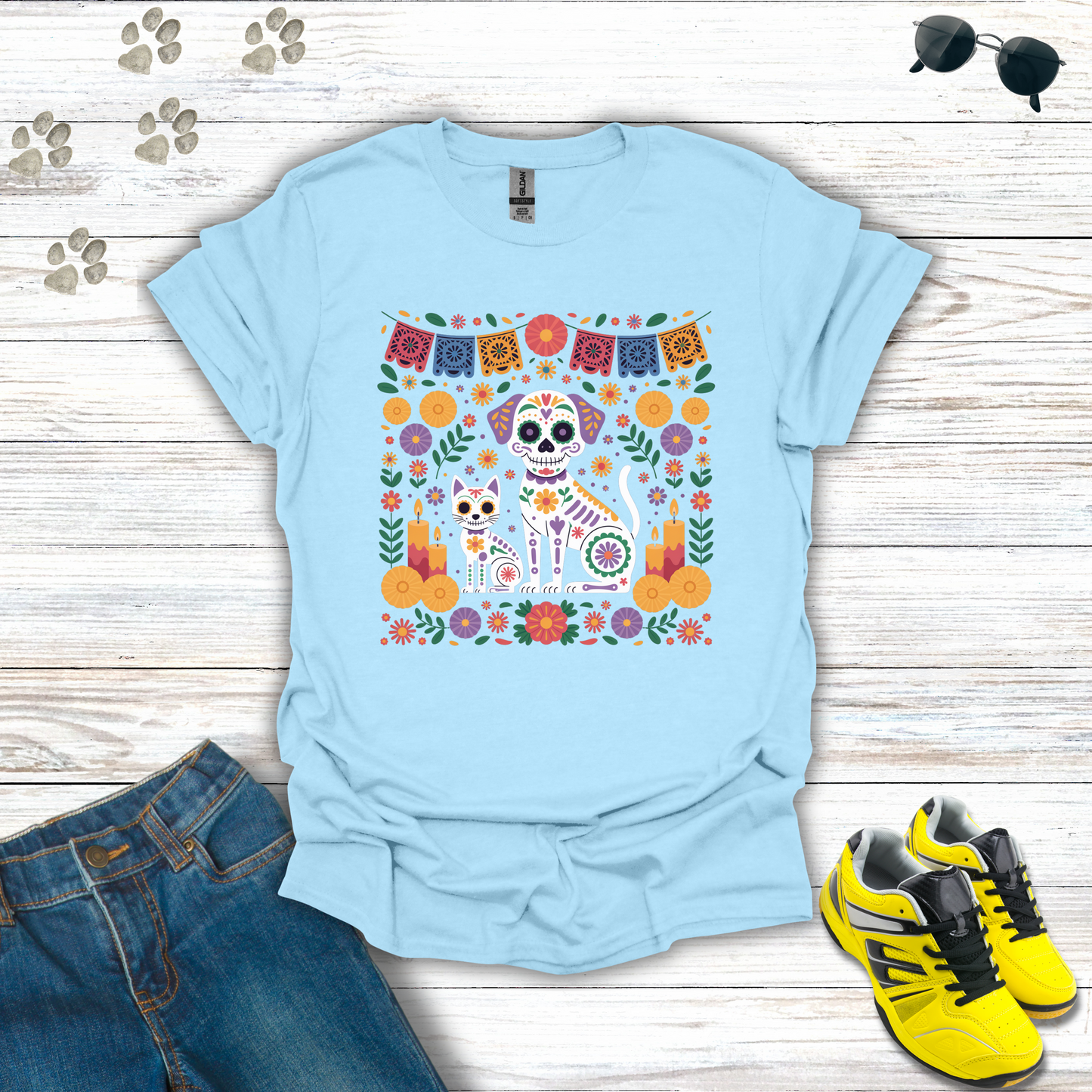 Light blue t-shirt with colorful graphic design on a wooden surface with jeans and sneakers.