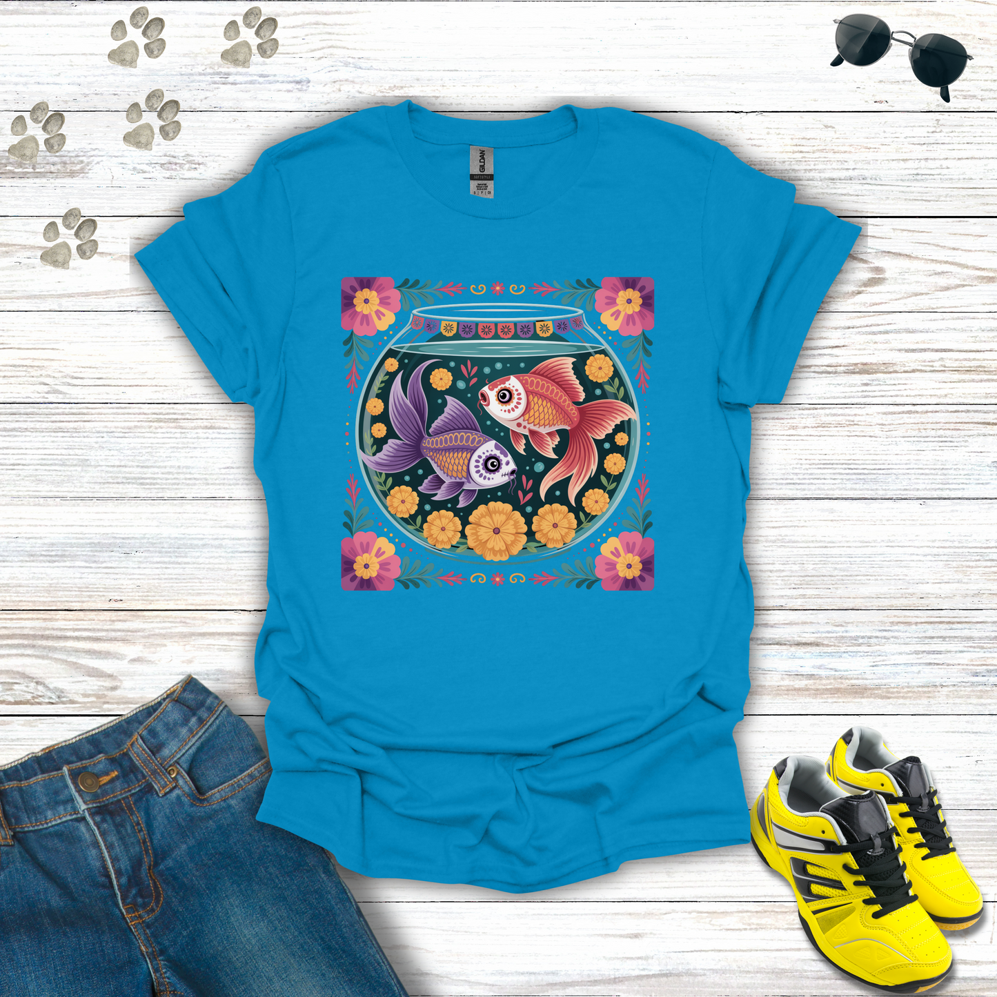 Sapphire t-shirt with fish bowl design on a wooden surface with jeans and sneakers.