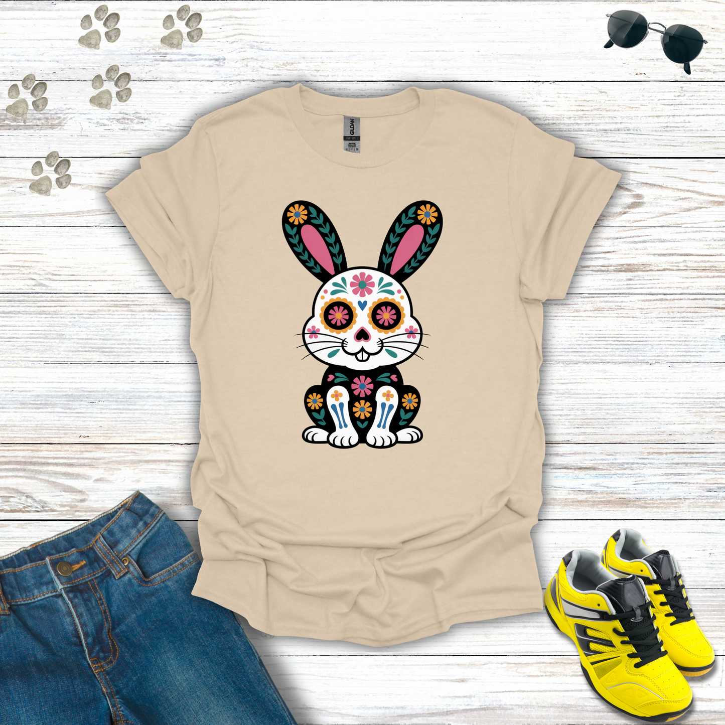 Sand t-shirt with a colorful bunny design, paired with jeans and yellow sneakers on a wooden surface.