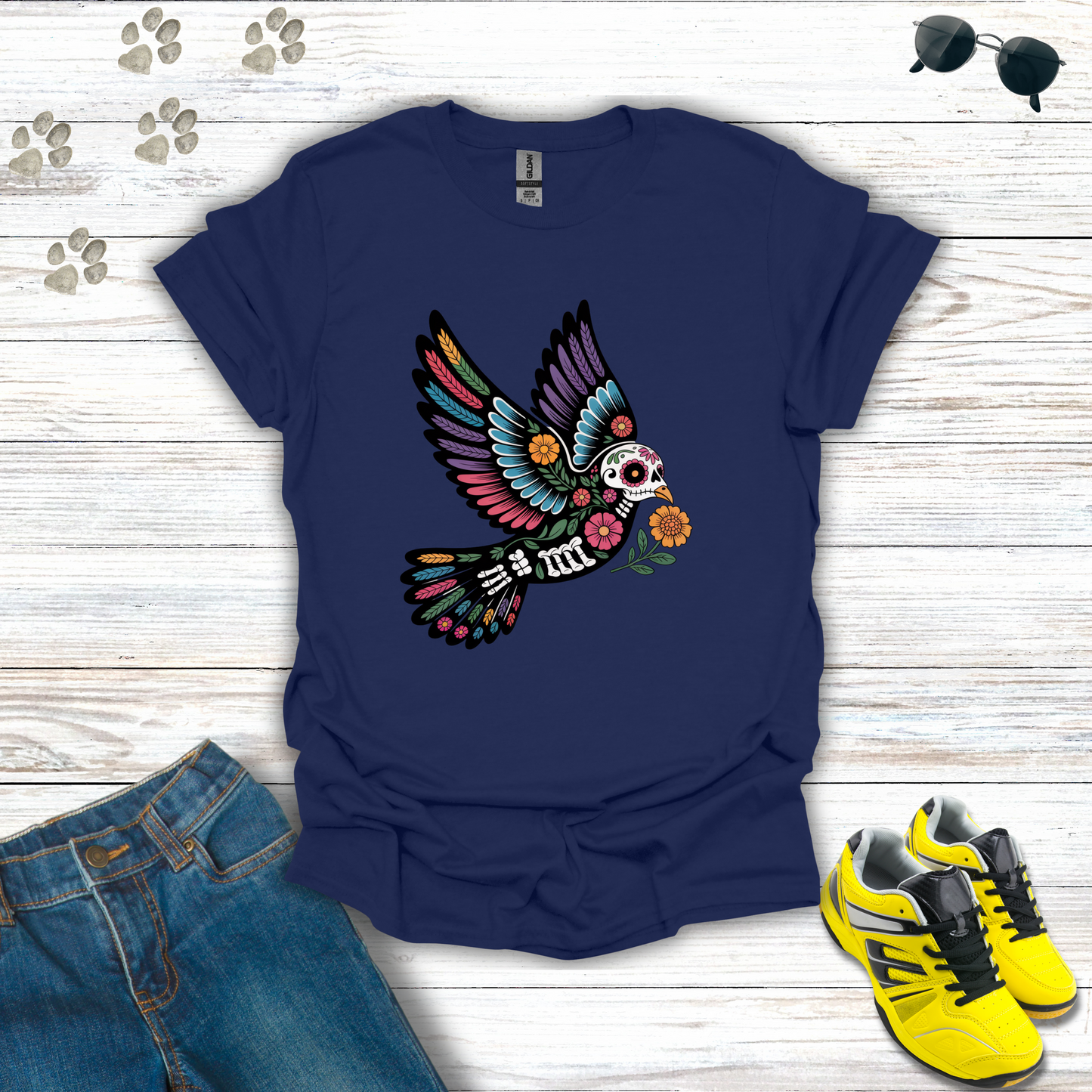 Navy blue t-shirt with colorful skeleton bird design on a wooden surface with jeans and sneakers.