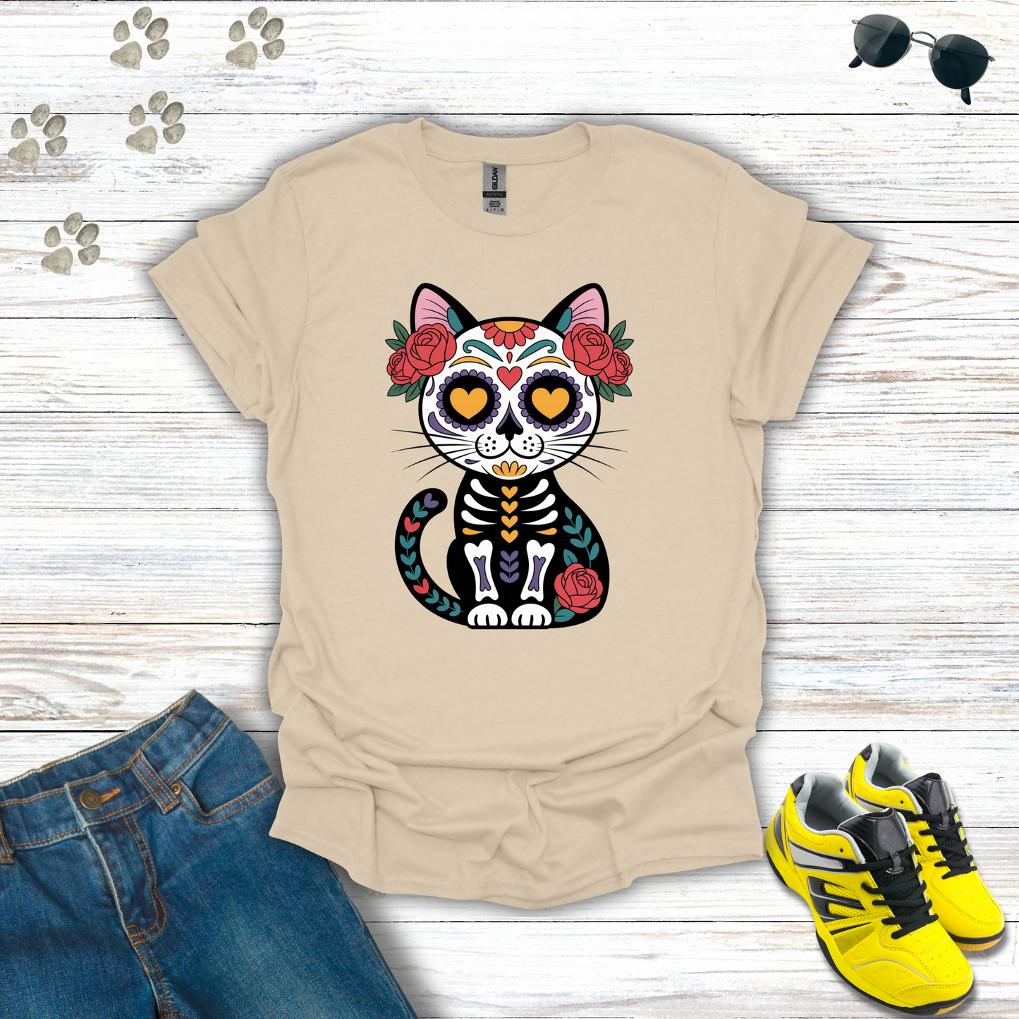 Sand t-shirt with a colorful cat skeleton design on a wooden surface with jeans and sneakers.