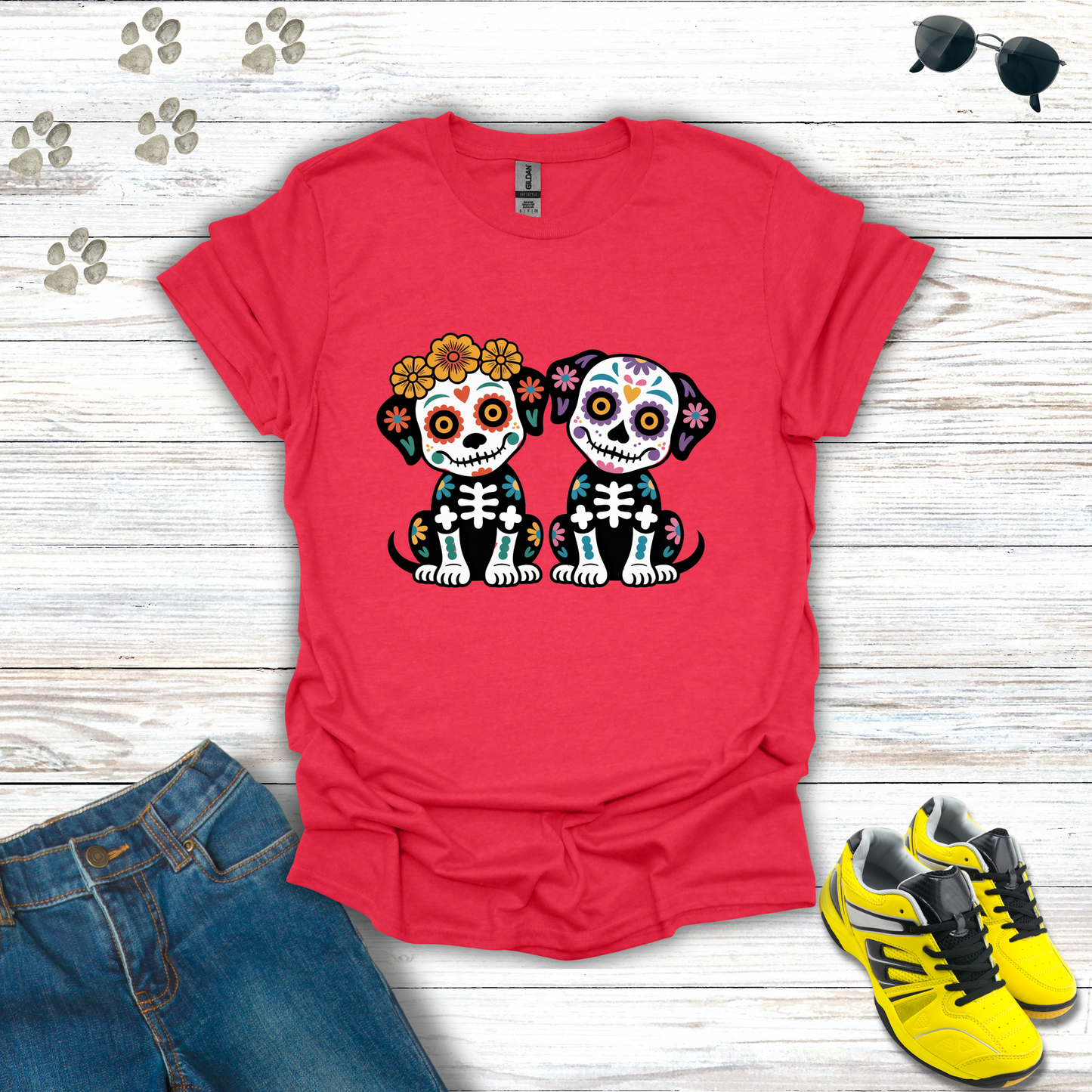 Heather Red t-shirt with skull design of two dogs, placed on a wooden surface with jeans and sneakers.