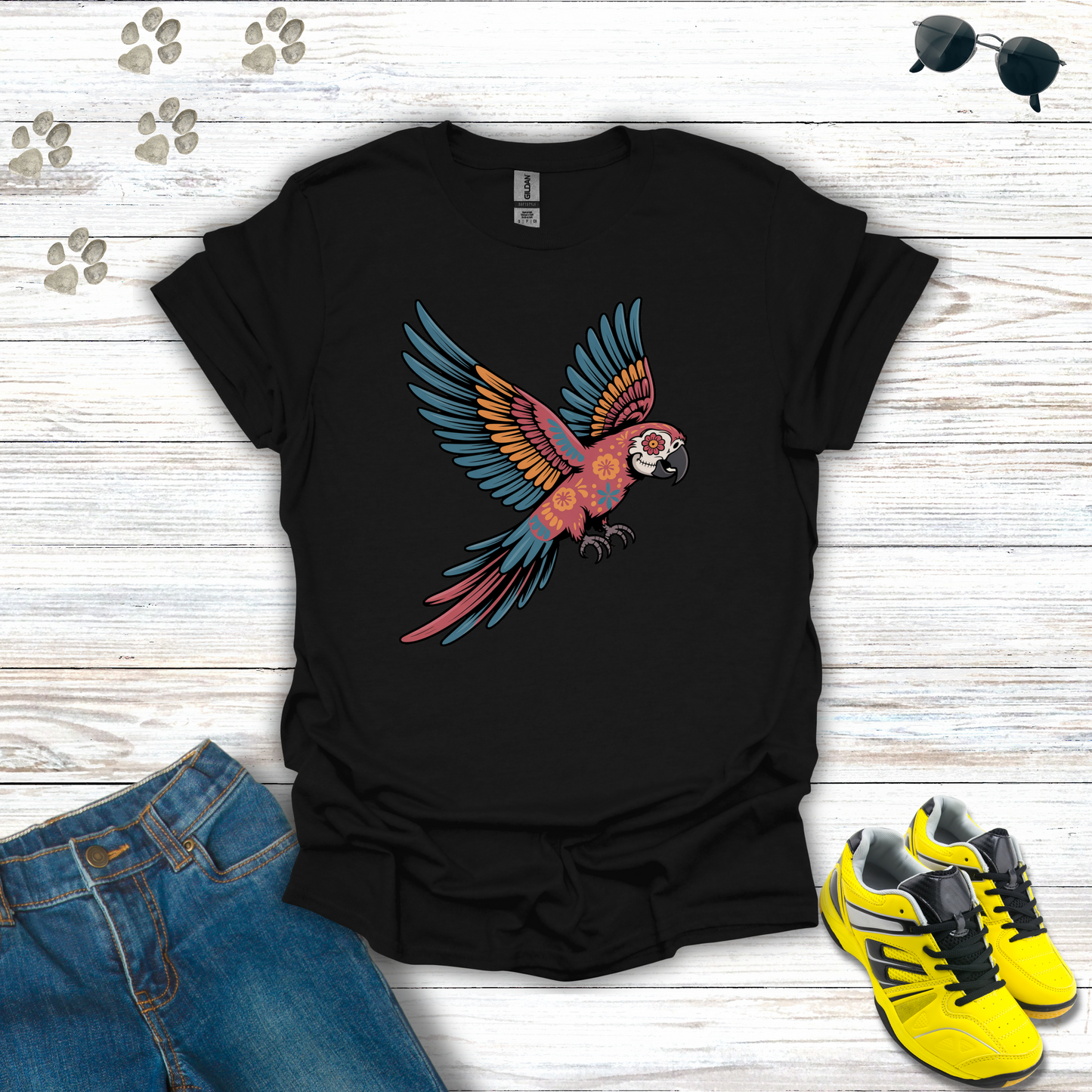 Black t-shirt with a colorful parrot design on a wooden surface with jeans and sneakers.