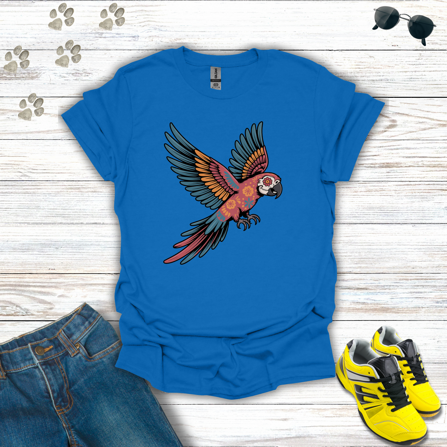 Royal t-shirt with a parrot design on a wooden surface with jeans and sneakers.