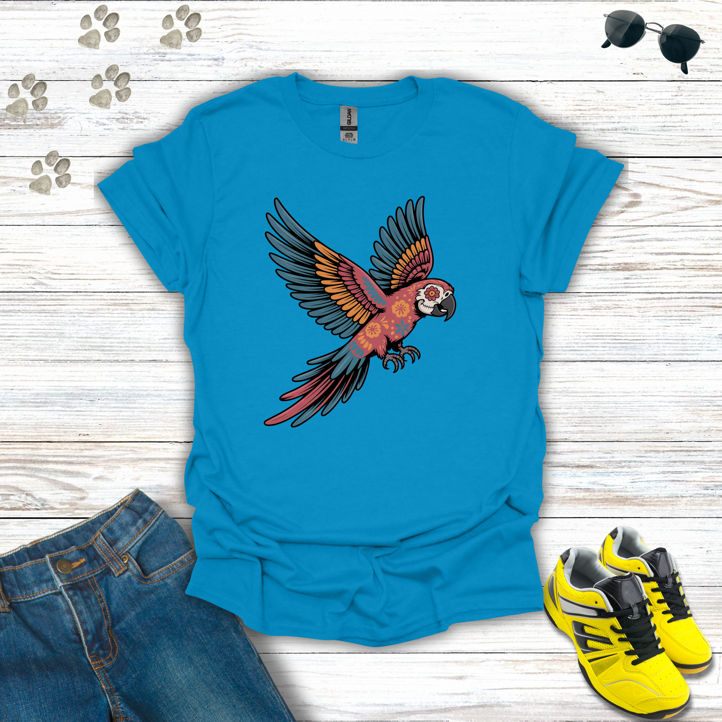 Sapphire t-shirt with a parrot design on a wooden surface with jeans and sneakers.