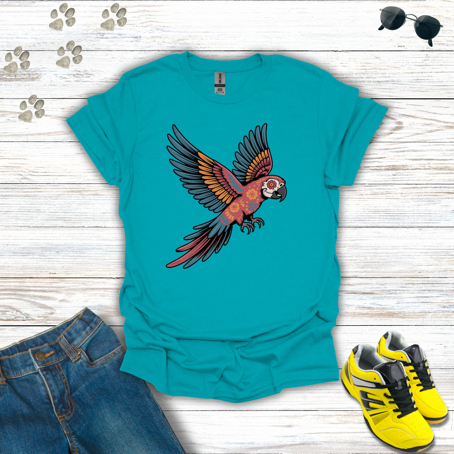 Tropical Blue t-shirt with parrot design on a wooden surface with jeans and sneakers.