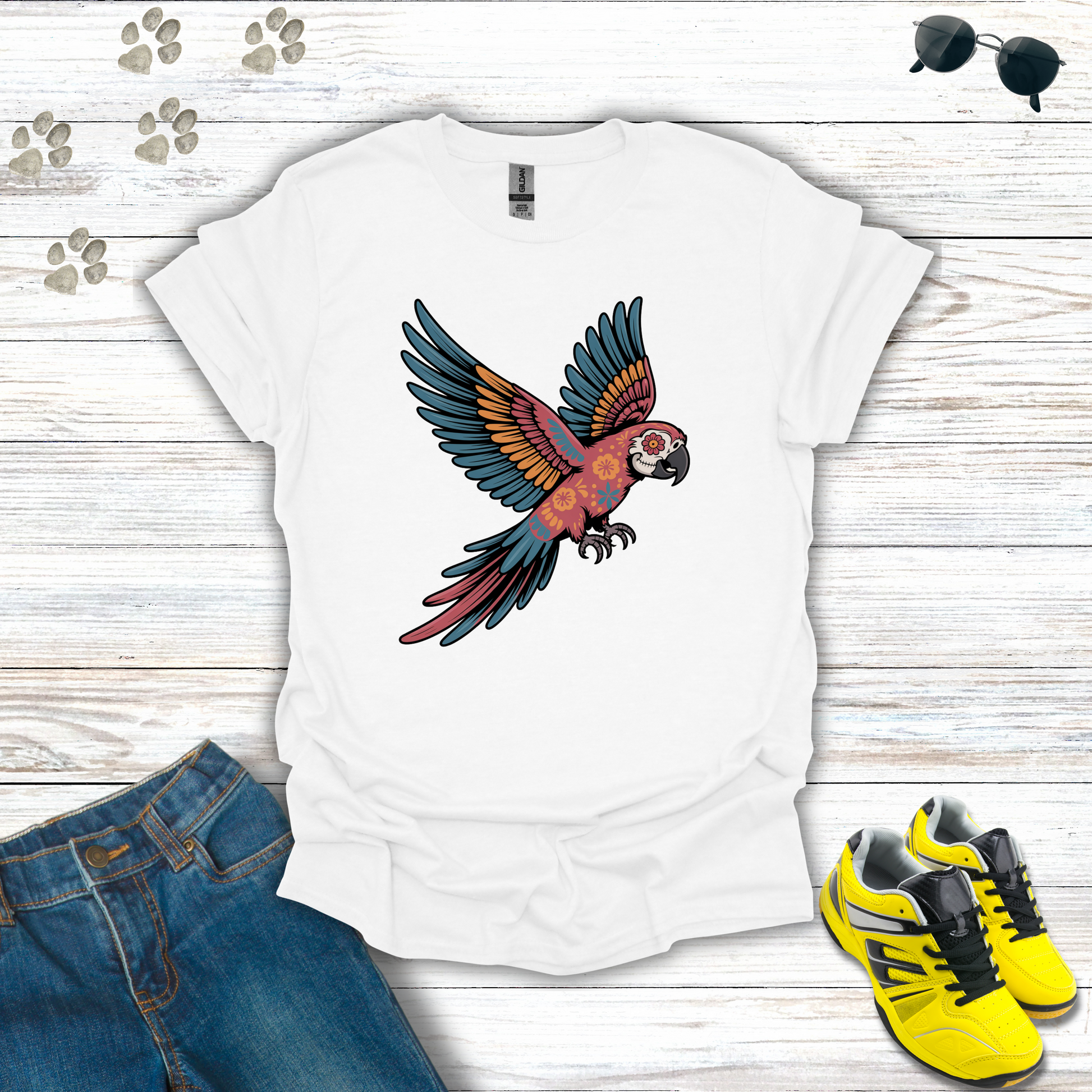 White t-shirt with a parrot design on a wooden surface with jeans and sneakers.
