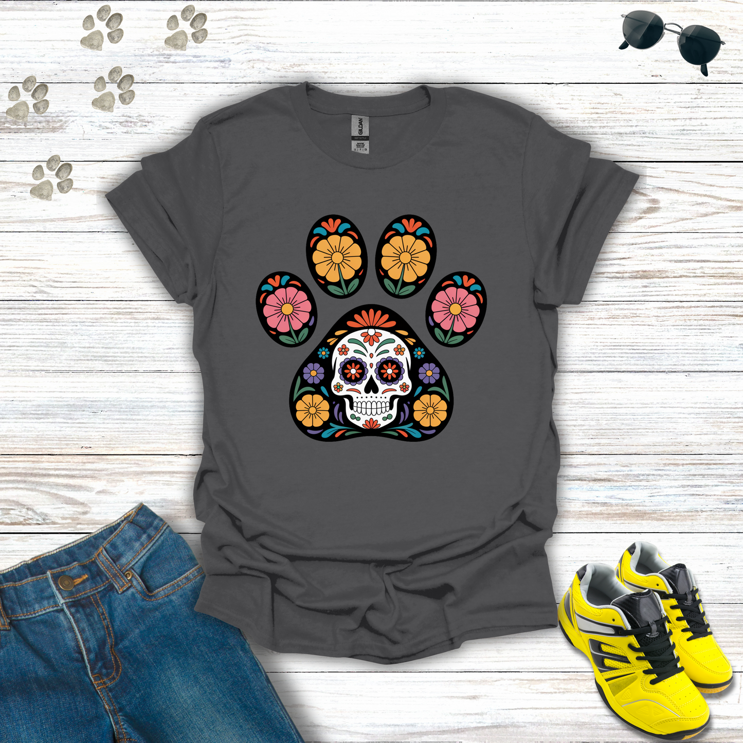 Charcoal t-shirt with colorful paw print design featuring a skull, placed on a wooden surface with jeans and sneakers.