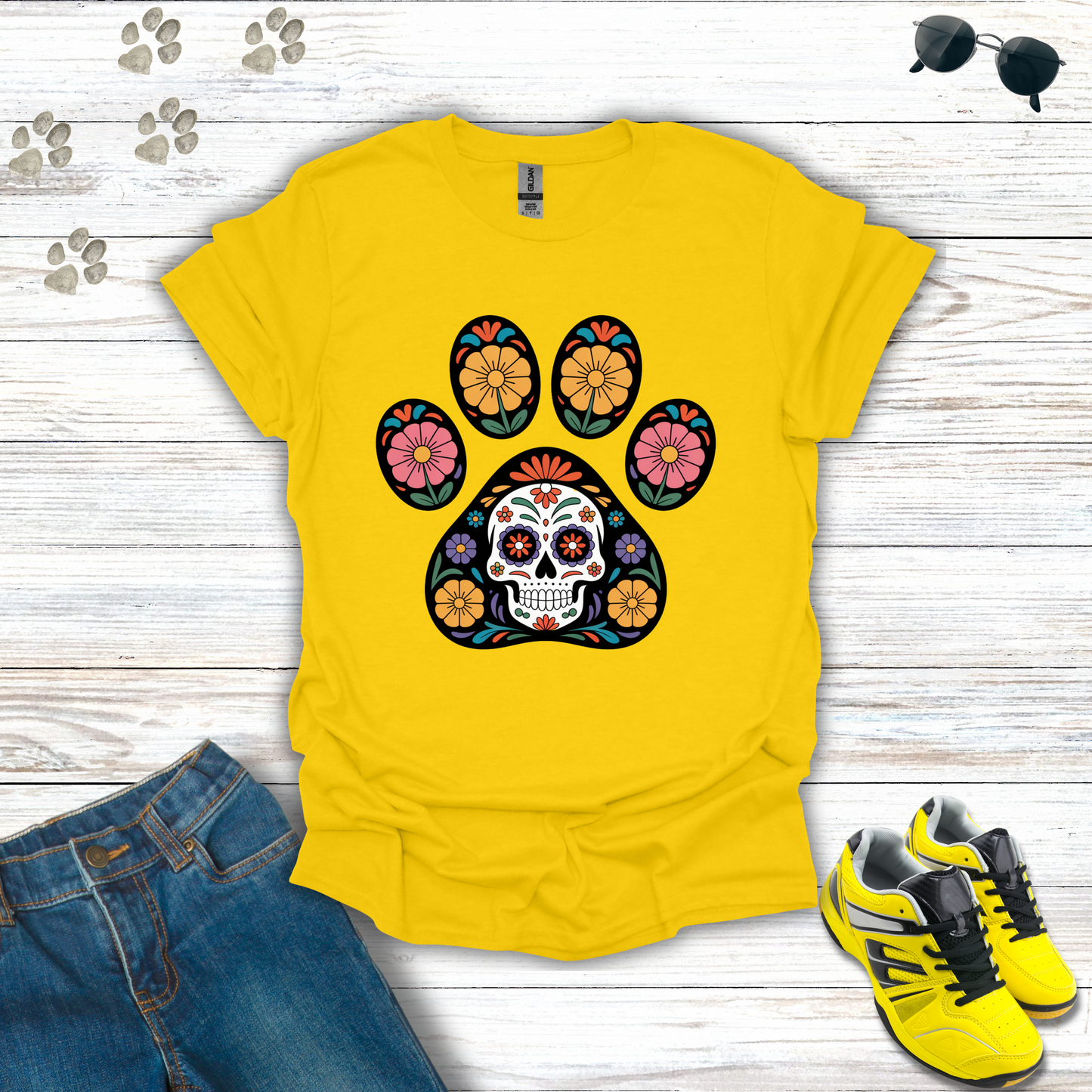 Daisy t-shirt with a colorful paw print design featuring a skull on a wooden surface with jeans and shoes.