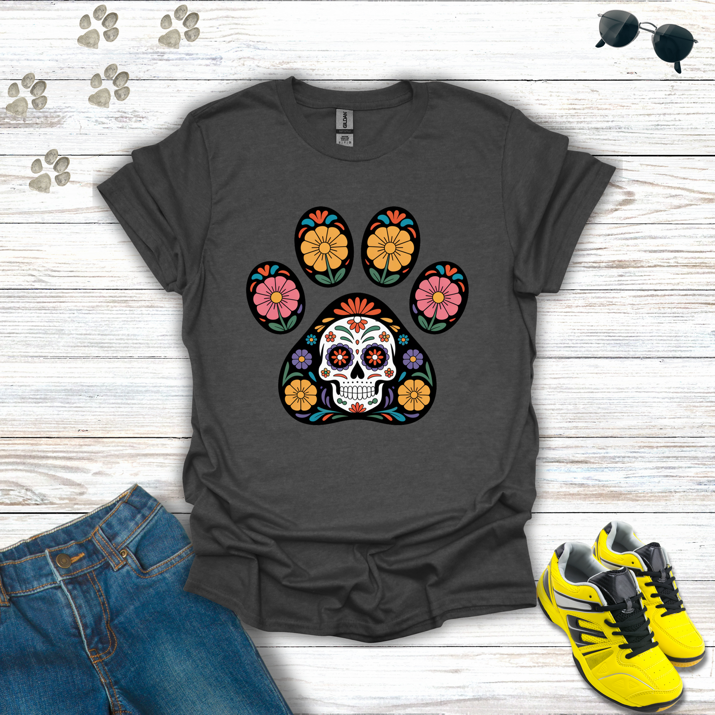 Dark Heather t-shirt with colorful paw print design featuring a skull, placed on a wooden surface with jeans and yellow sneakers.