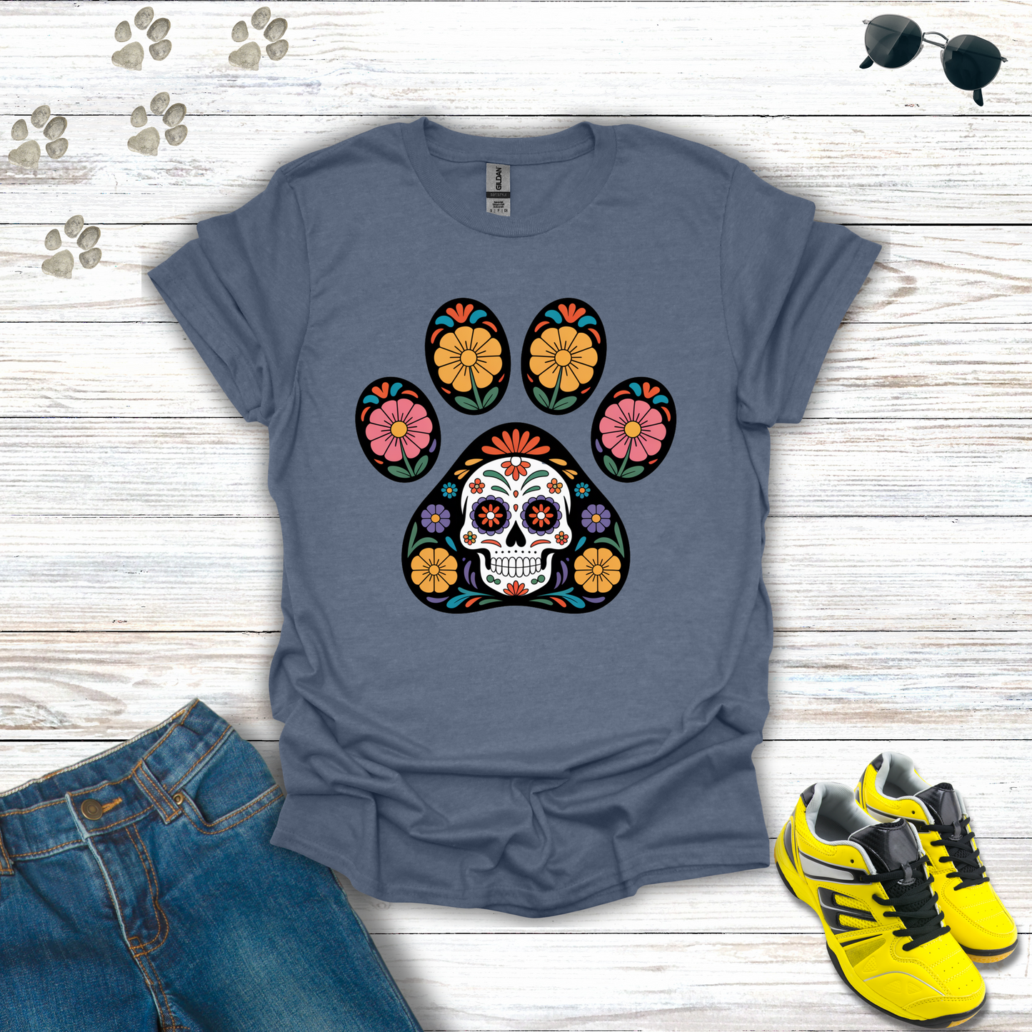 Heather Indigo t-shirt with a colorful paw print design featuring a skull, accompanied by jeans and yellow sneakers on a wooden surface.