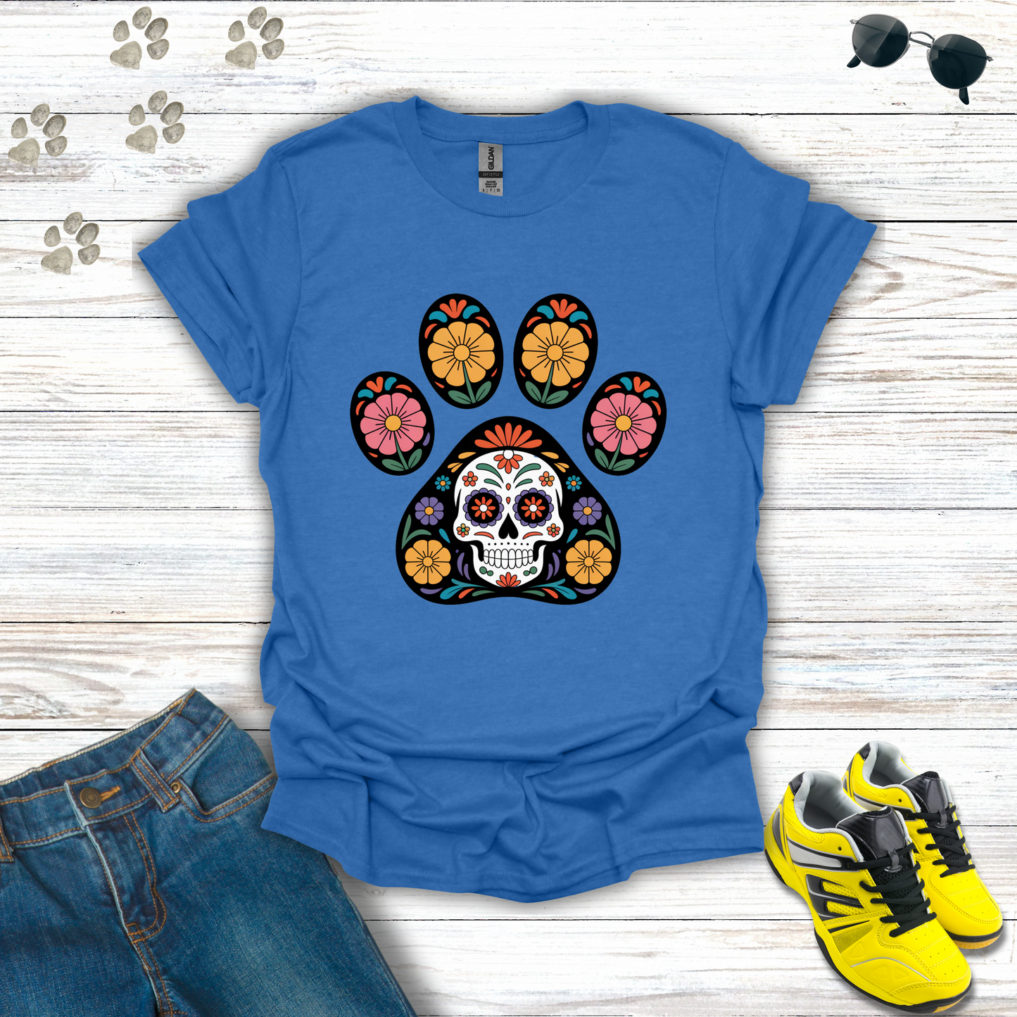 Heather Royal t-shirt with colorful paw print design featuring a skull, placed on a wooden surface with jeans and sneakers.