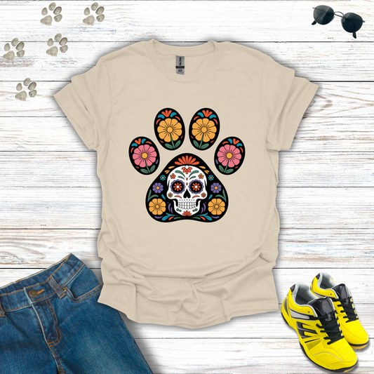 Natural t-shirt with colorful paw print design featuring a skull, surrounded by jeans and yellow sneakers on a wooden surface.