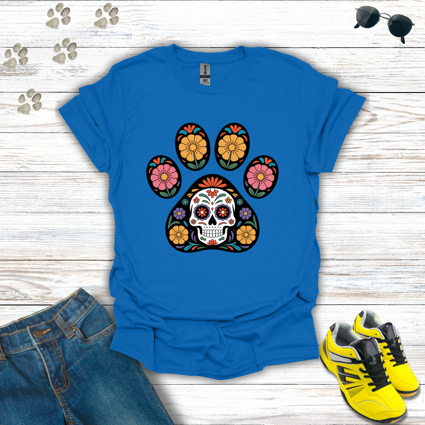 Royal t-shirt with colorful paw print design featuring a skull, paired with jeans and sneakers on a wooden surface.
