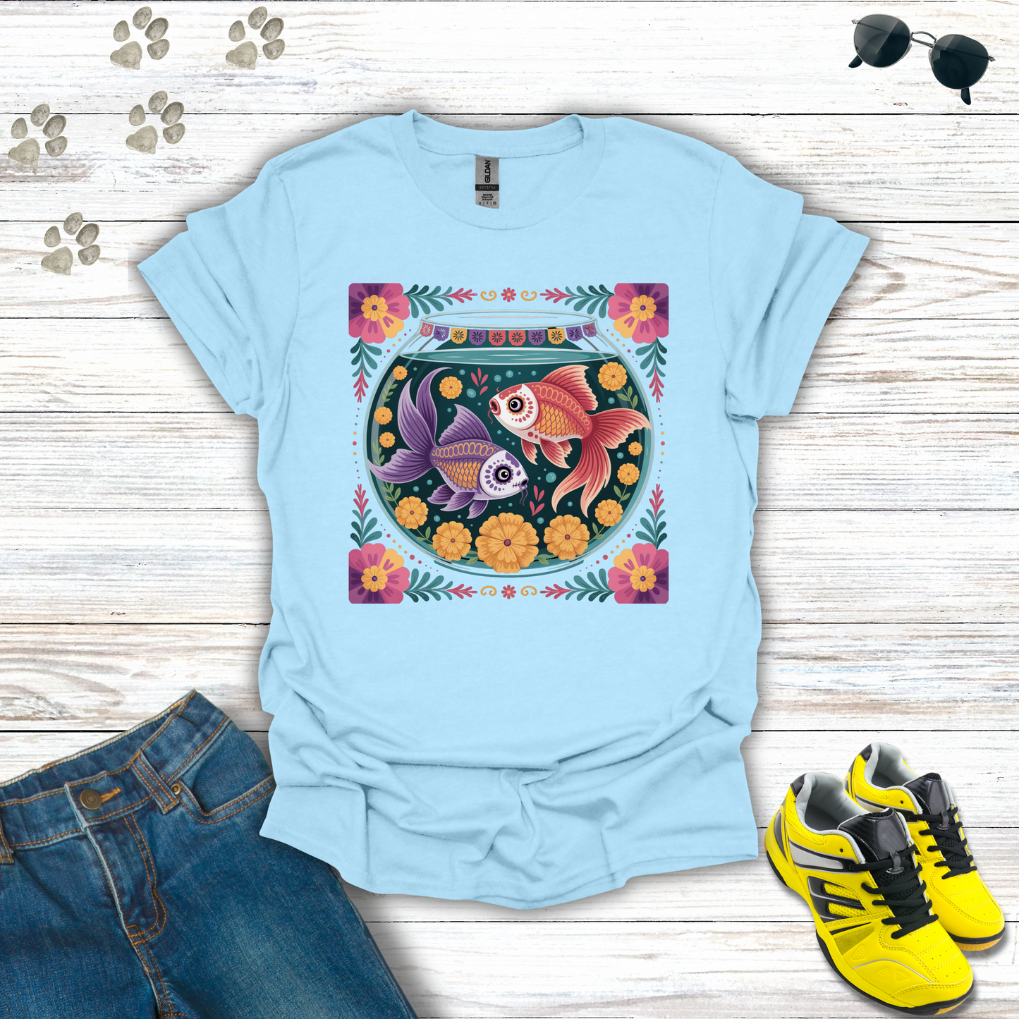 Light blue t-shirt with fish design on a wooden surface with jeans and sneakers.