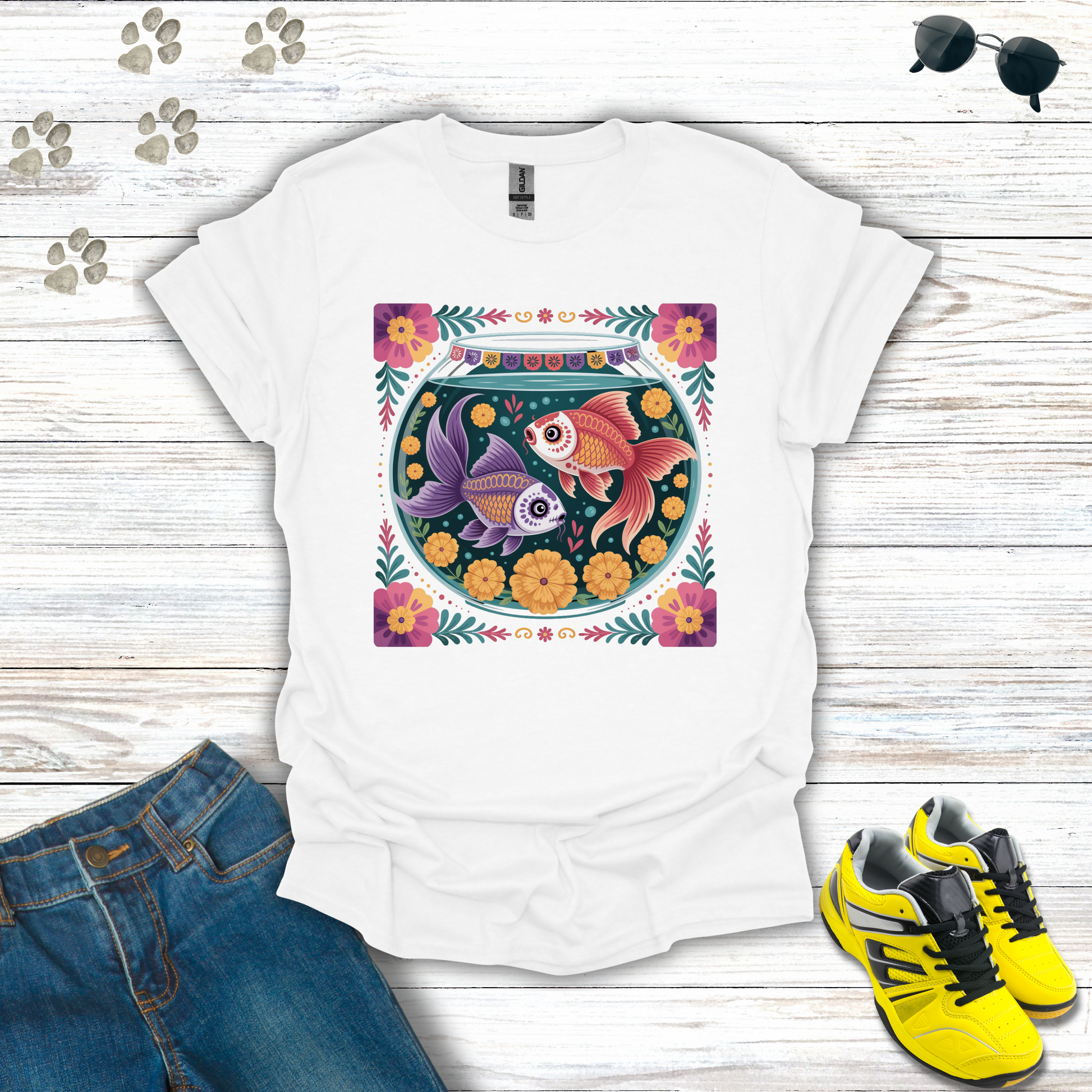 White t-shirt with fish bowl design on a wooden surface with jeans and sneakers.