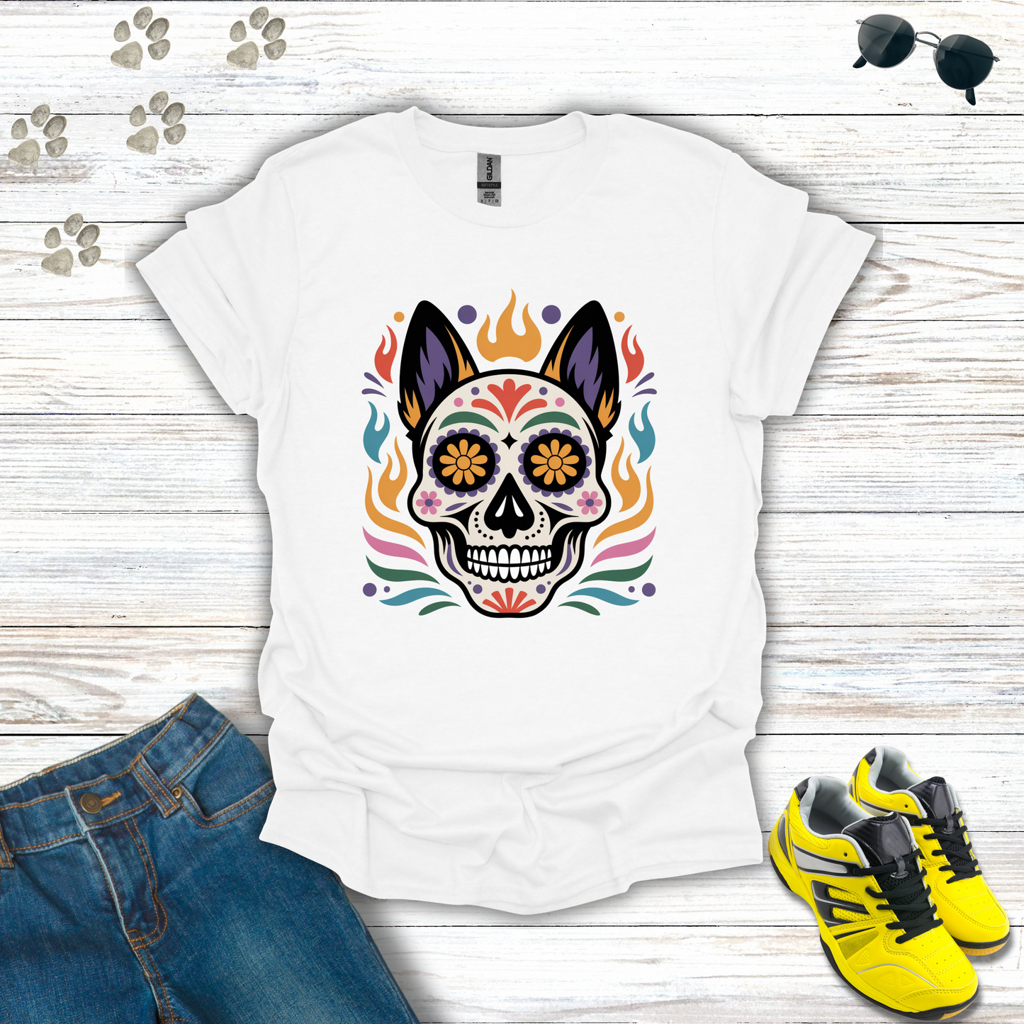 White t-shirt with colorful skull design on a wooden surface with jeans and sneakers.